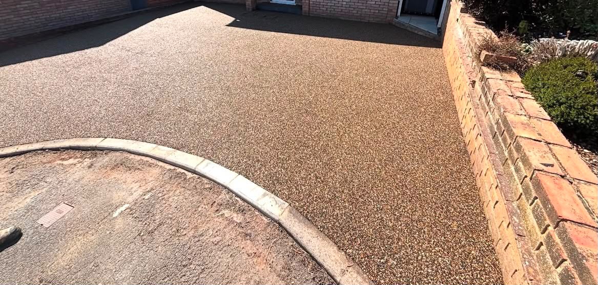 Golden resin driveway with curved edging beside a brick garden wall