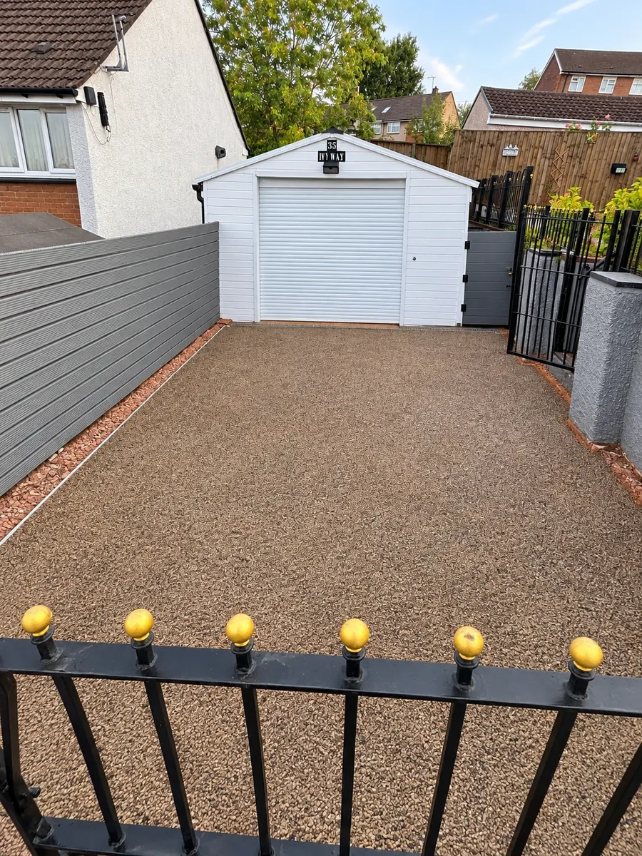 Resin driveway beside white garage, grey boundary fence and metal gate