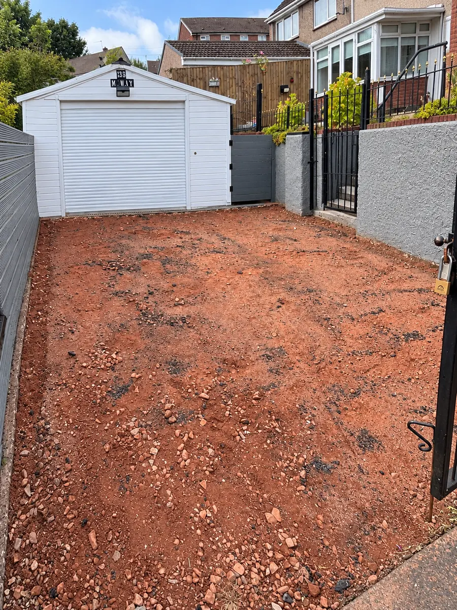 Driveway ground preparation beside white garage and grey boundary fence
