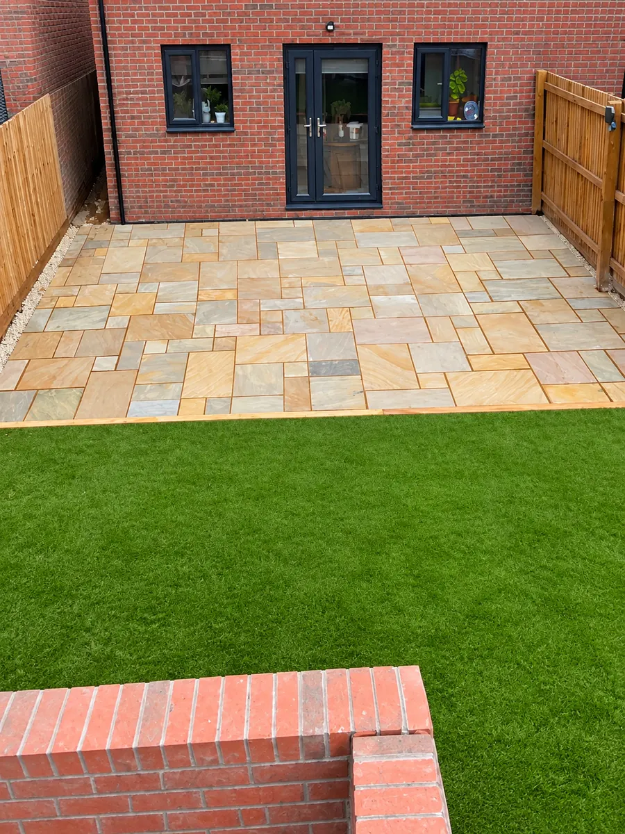 Sandstone patio with artificial lawn outside black rear doors