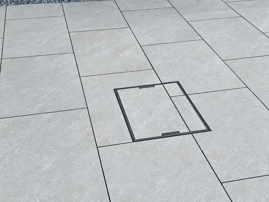 Close view of grey slabs and recessed utility access cover; cover alone is not proof of drainage installation
