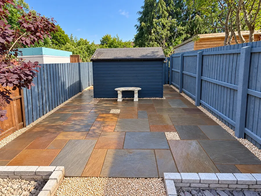 Sandstone patio, gravel inset and blue timber fencing beside shed