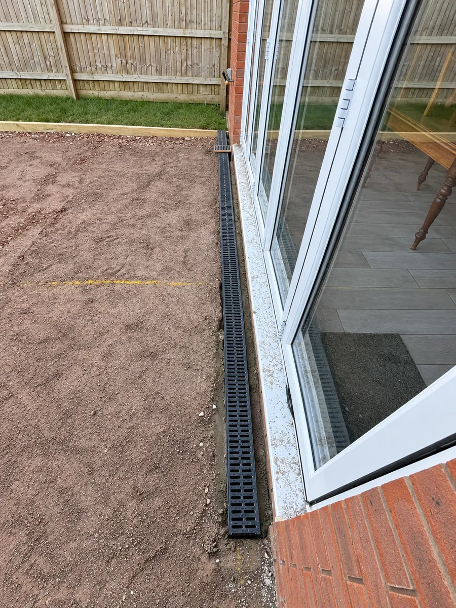 Linear channel drain beside glazed doors during patio construction